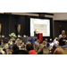 A gentleman speaks at a podium to a full ballroom 