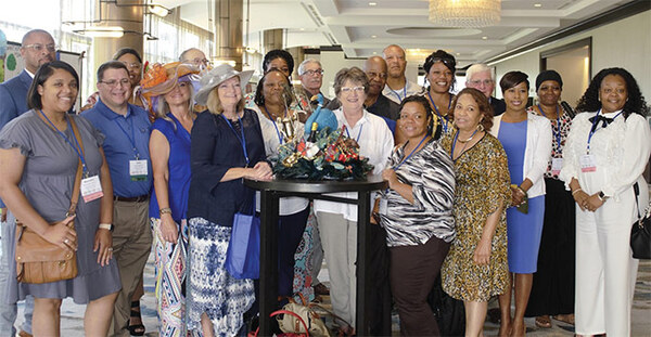 A group of people standing around a table with a beautifully decorated hat on it
