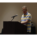 a man in a striped polo speaking at the podium 