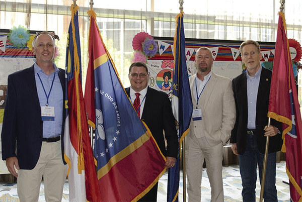 four men standing together each holding their state\'s flag