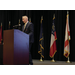 a man standing at a podium speaking with various flags behind him 