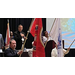 A woman singing the national anthem while a group of people hold various military flags