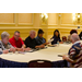 Men and women smile, as they are seated around a table while looking at papers.