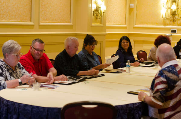 Men and women smile, as they are seated around a table while looking at papers.