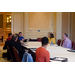 Men and women seated around a table listen as the man at the head of the table speaks.