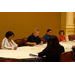 Men and women listen and take notes as they are seated around the table. 