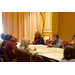 Men and women listen as they are gathered around the table. 