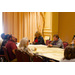 Men and women listen and talk with each other as they are gathered around the table. 