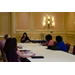 The woman at the head of the table speaks to those seated around the table.