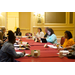 Men and women are seated around a table taking notes.