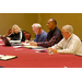 A woman and three men sit at a table taking notes.