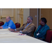 Two men and a woman sit at a table, listening to a speaker.