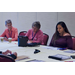 Three women sit behind a table and take notes.