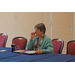 A woman sits at a table and listens to someone speaking. 