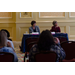 Two women sit behind a table and listen intently.