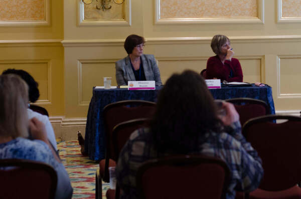 Two women sit behind a table and listen intently.