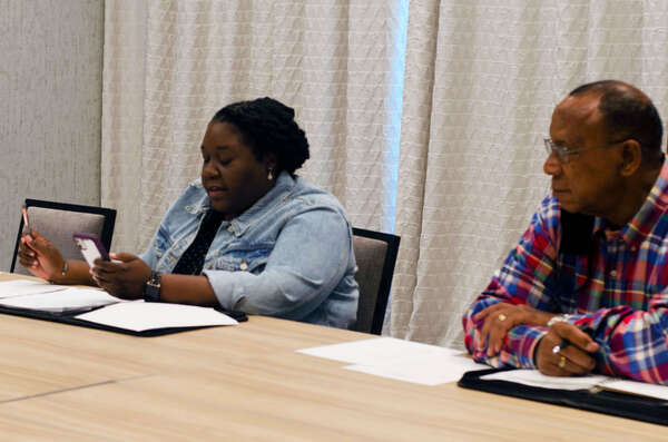 A woman and a man sit at a table together as she reads something from the cell phone in her hand. 