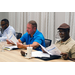 Three men sit at a table, reading packets of paper together.