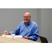 A man sits, taking notes at a table and smilling.