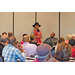 A woman wearing a hat stands to address the room. 