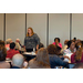 A woman stands and speaks to those seated around her. 