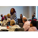 A woman stands and looks to her left while she is speaking to people in the room.