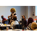 A woman stands and speaks to those sitting in the room. 