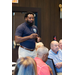 A bearded man stands and speaks using hand motions.