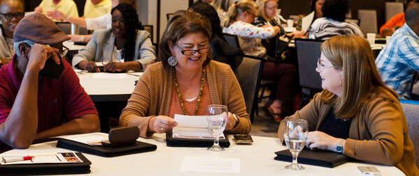 A man and two women sit at a table together smiling and laughing.