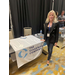 A woman standing in front of a table with a table cloth that says The Clear Blue Company.