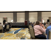 A group of people at multiple tables listening to a speaker who is talking behind a podium. 