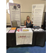 A woman sitting behind a booth table for the Nelrod Company.