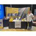 A woman standing proudly in front of a booth display for Precision Concrete Cutting.