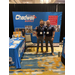 Two men standing side by side in front of a booth for Chadwell Supply. 