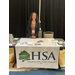 A woman smiling boldly behind a booth table for Housing Solutions Alliance. 
