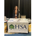 A woman smiling boldly behind a booth table for Housing Solutions Alliance.