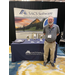 A man stands with his arms behind his back in front of the SACS Software table. 