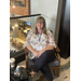 A woman sits cross legged in a chair while smiling. 