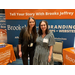 Two women pose together in front of a booth for Brooks Jeffrey Marketing. 