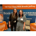 Two women pose together in front of a booth for Brooks Jeffrey Marketing.