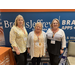 Three blonde ladies pose together in front of the Brooks Jeffrey Booth. 