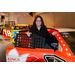A women standing next to a race car smiling.