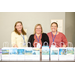 Three women smiling with gift bags in front of them.