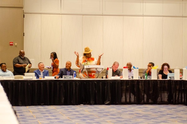 Woman in an orange and white top with slacks standing at the podium for the Executive Committee meeting.
