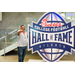  Man in a gray shirt pointing toward the camera at the Executive Committee dinner in front of a Chick-fil-a sponsored College Football Hall of Fame sign. 
