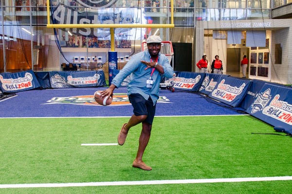A gentleman in a hat standing on one leg while he poses with a football.