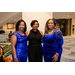  Three women in dresses stand and smile for a photo. 