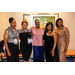  Five women in elegant outfits stand and smile for a photo. 