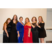  Six women in dresses stand in a line and smile for a photo. 