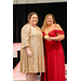  Two woman stand and smile for a photo. One is holding a GOAT award. 
